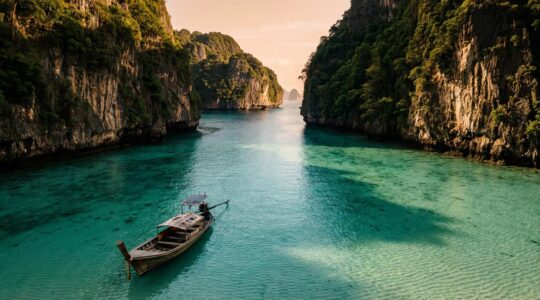 Bateau longtail traditionnel isolé ancré dans une crique turquoise déserte entourée de falaises verdoyantes