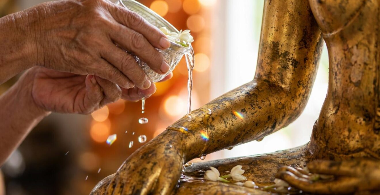 Mains versant délicatement de l'eau parfumée avec des pétales de jasmin sur une statue dorée de Bouddha