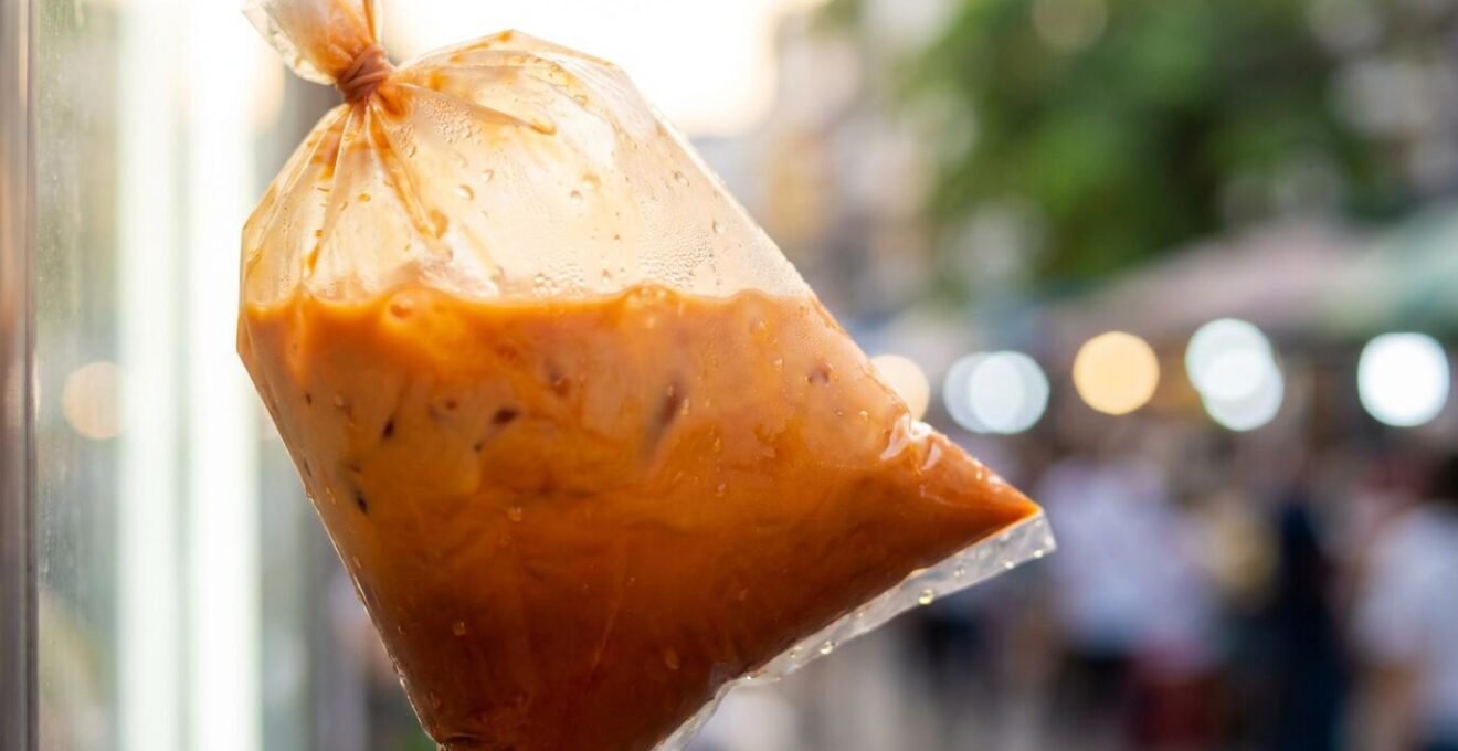 Gros plan sur un sac plastique contenant une boisson colorée avec paille et élastique