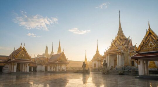 Vue majestueuse d'un temple royal thaïlandais avec toits dorés et statues de gardiens, baigné dans la lumière dorée du matin